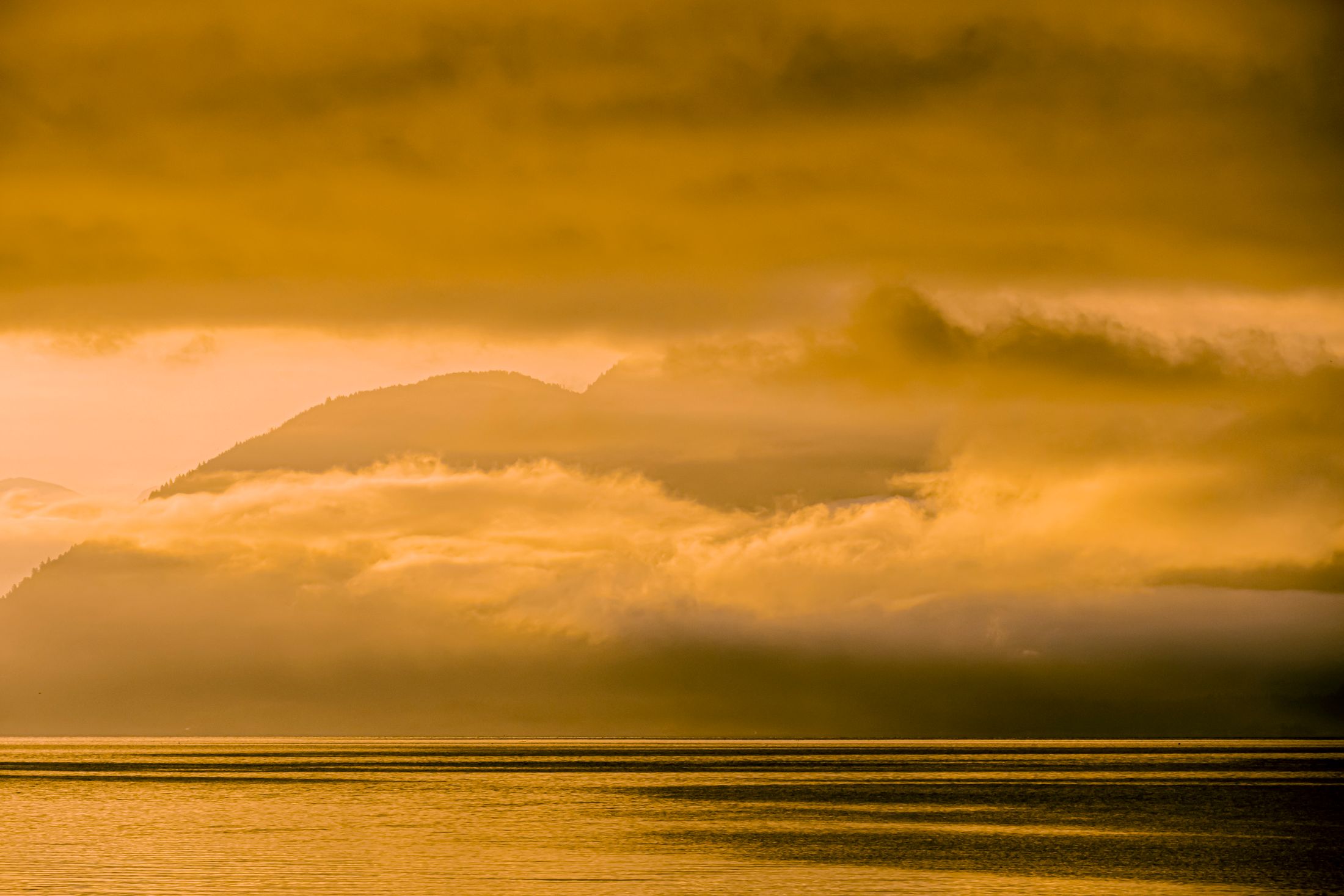 Montagne et nuages baignés de lumière dorée au-dessus de l'eau