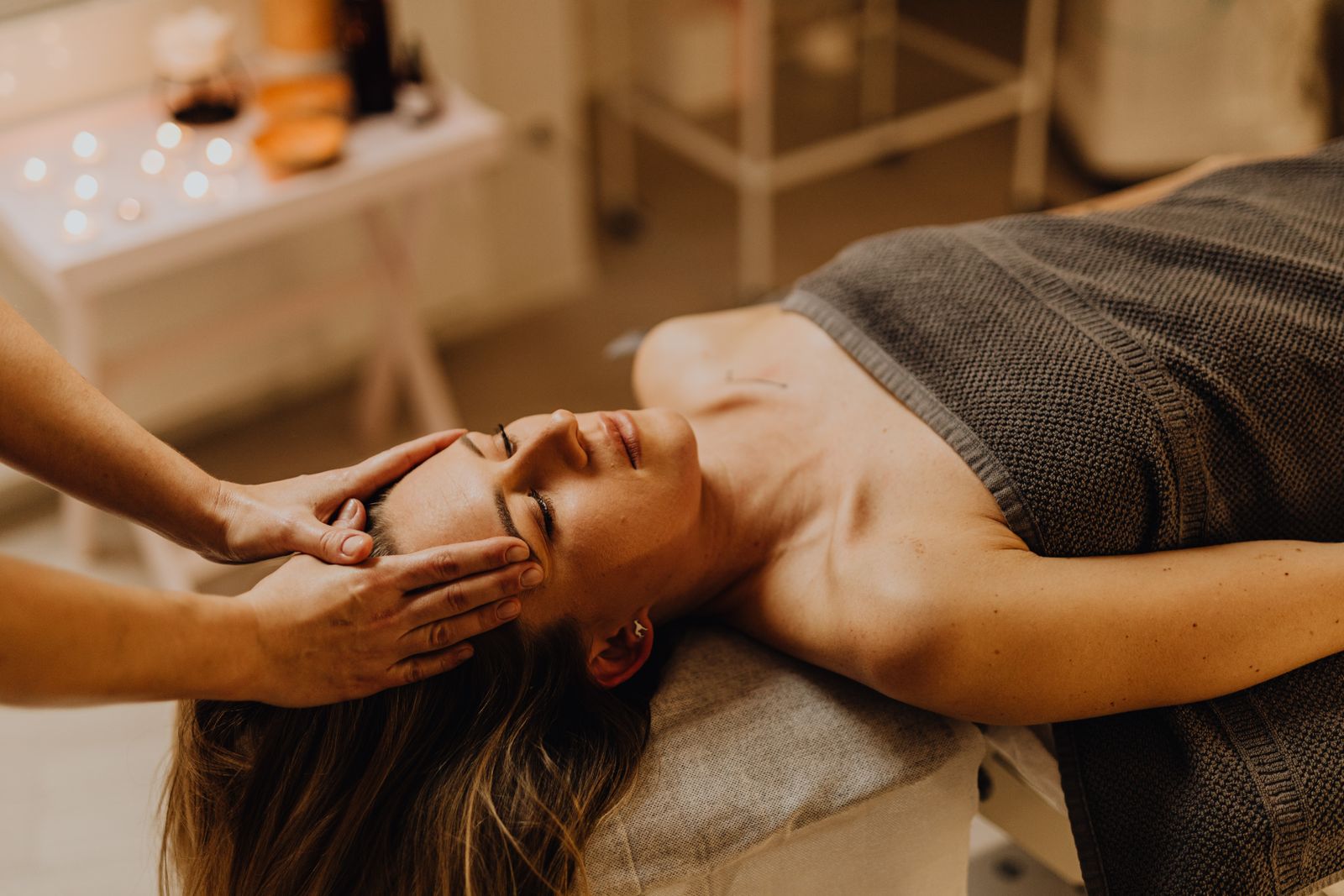 Une femme allongée sur une table de soin, les yeux fermés, pendant que deux mains se posent doucement sur son front et sur le côté de sa tête